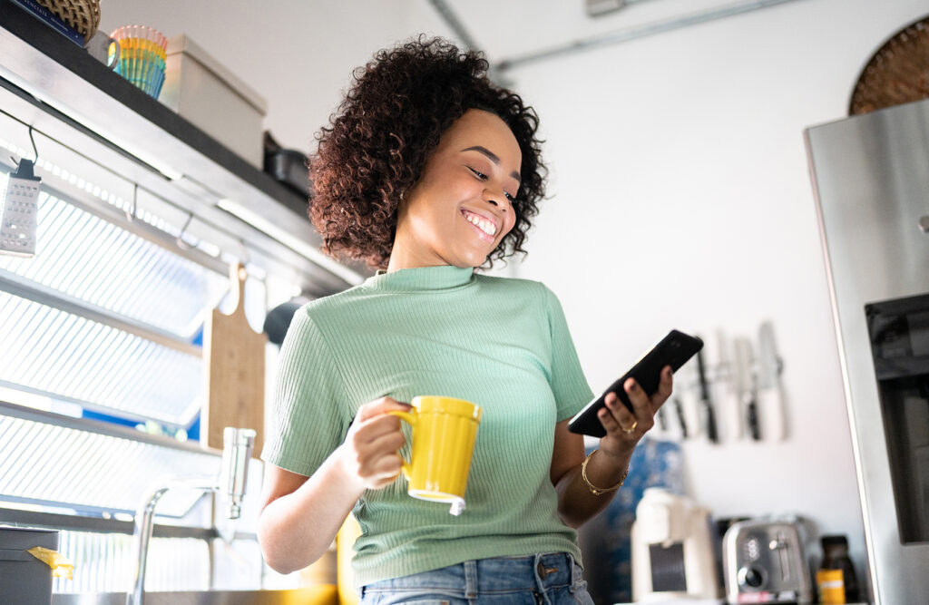 Young woman holding a mug and using smartphone at home